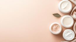 four-jars-of-cosmetic-cream-in-different-shades-arranged-on-a-pink-background-with-a-draped-shimmering-fabric-and-a-single-dried-leaf-photo